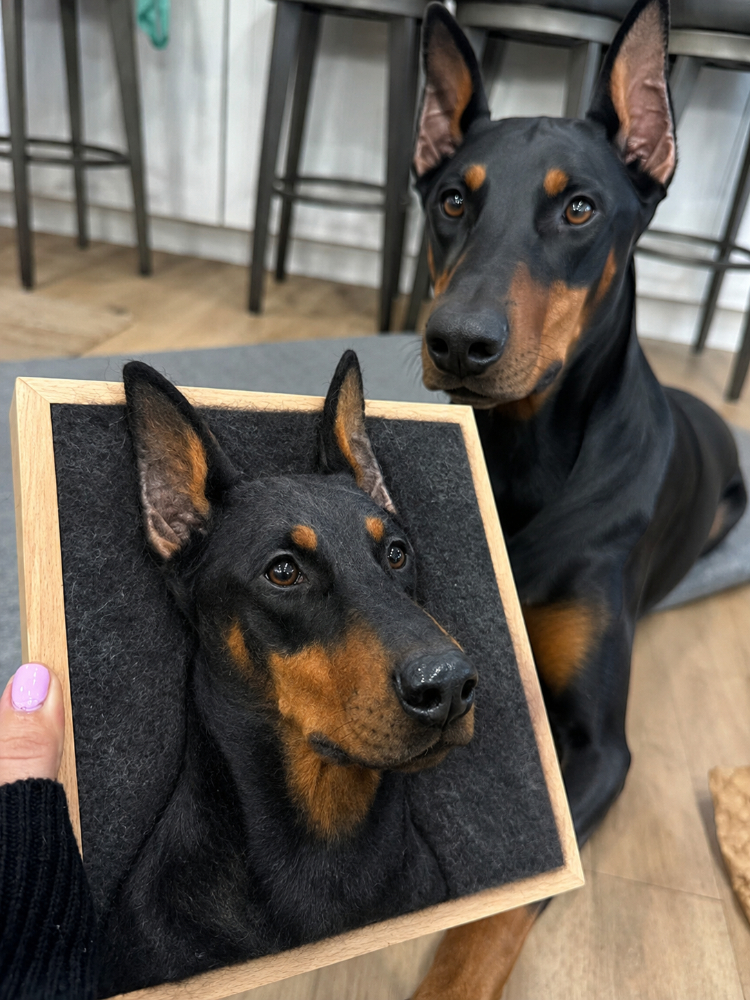 A real dog beside a handcrafted wool portrait